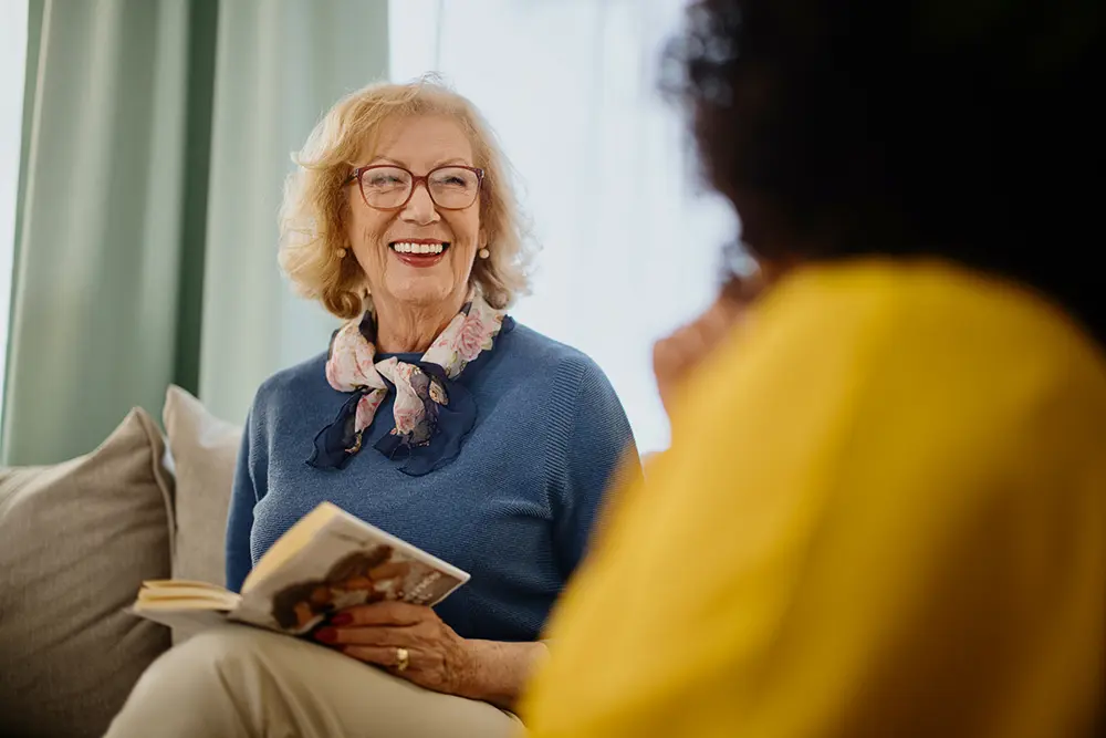 Senior woman reading a book on a sofa with a friend